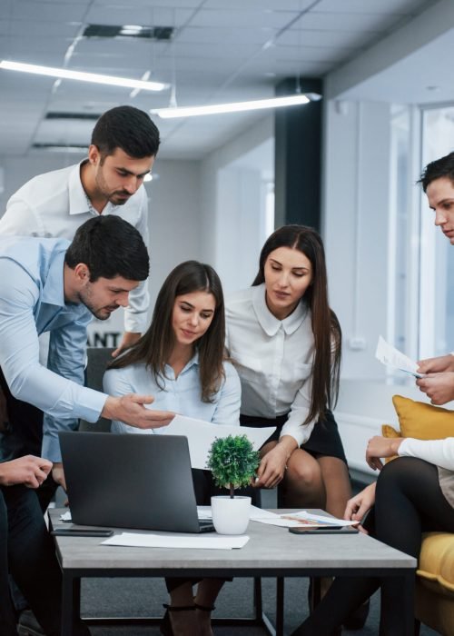 Guy shows document to a girl. Group of young freelancers in the office have conversation and working.